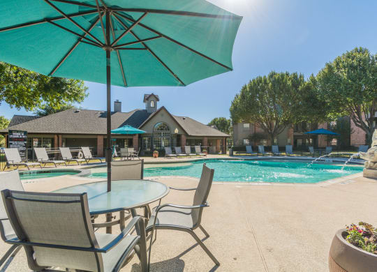 pool and patio with chairs and umbrellas at Fountains of Denton in Denton, TX