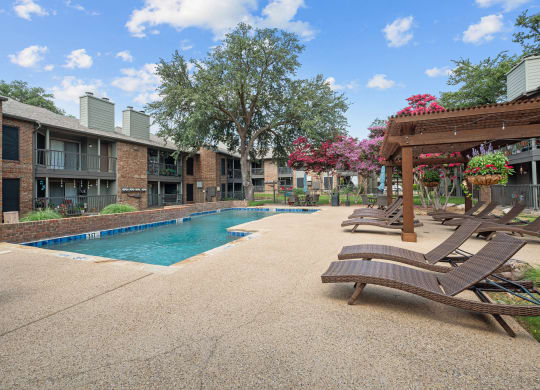 a swimming pool with chaise lounge chairs and a pergola in front of a brick
