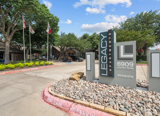 a sign that says Legacy Apartments at the entrance to a parking lot with flags in the background