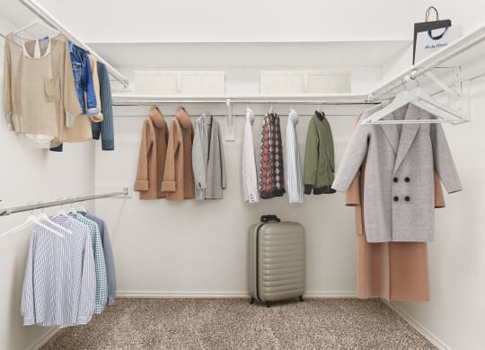 a closet with clothes hanging on a rack and a suitcase