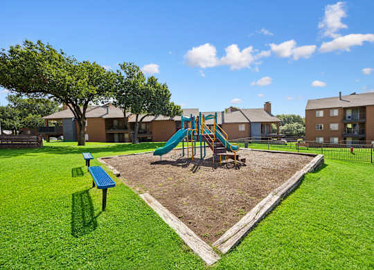 A playground with a green slide and a brown tree.