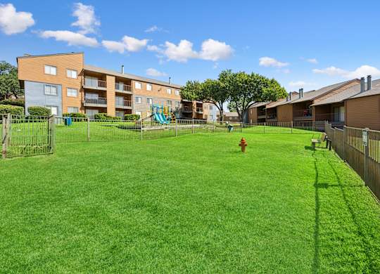 A large grassy area in front of apartment buildings with a playground and a fire hydrant.