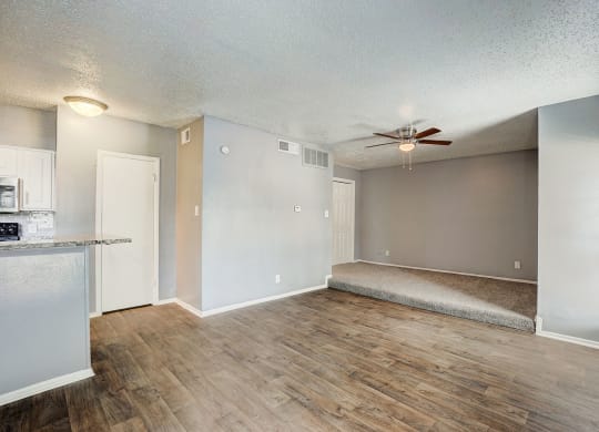 an empty living room and kitchen with a ceiling fan