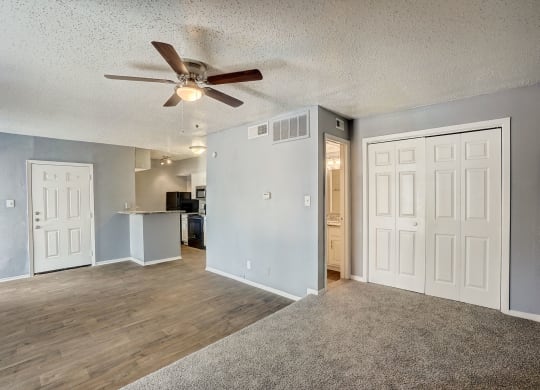 an empty living room with a ceiling fan and a kitchen