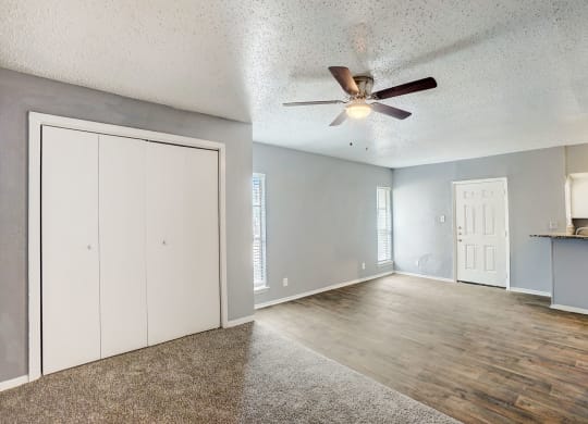 an empty living room with a ceiling fan and a door to the kitchen