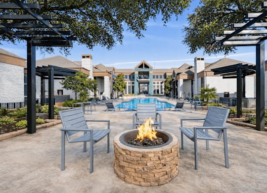 A fire pit sits in the middle of a patio with chairs around it.