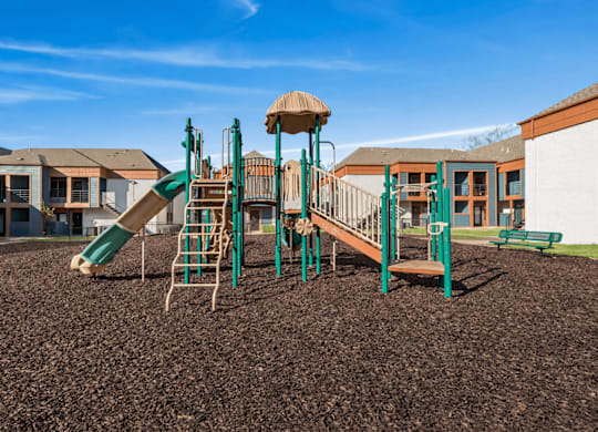 A playground with a green slide and a brown sandbox.