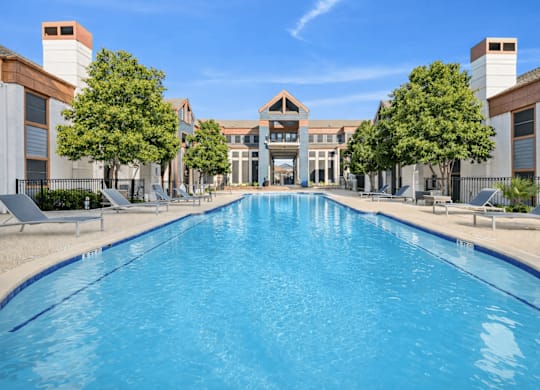 A large swimming pool in front of a building with trees on the side.
