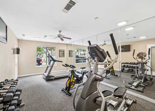 A gym with a variety of exercise equipment including treadmills, stationary bikes, and weight machines.