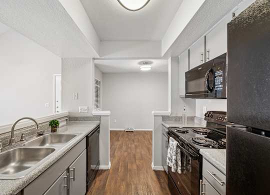 A kitchen with a stainless steel sink and black appliances.