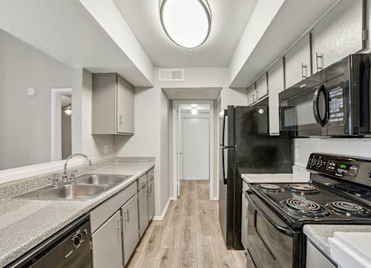A kitchen with black appliances and a wooden floor.