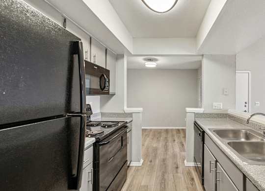 A black refrigerator is in a kitchen with wood floors and stainless steel appliances.