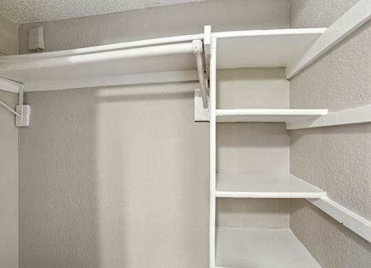 A white shelving unit with four shelves is mounted on a white wall.