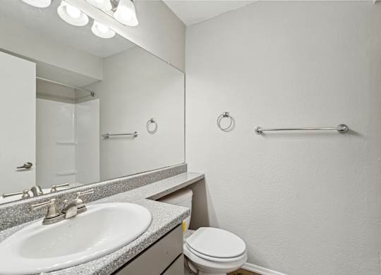 A bathroom with a toilet, sink, mirror, and towel rack.