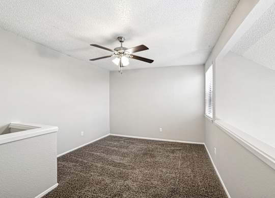 A room with a ceiling fan and carpeted floor.