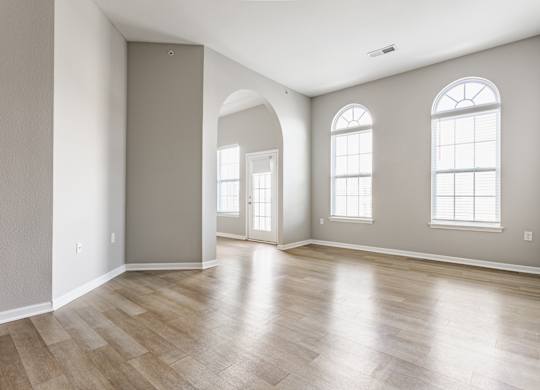 A room with wooden flooring and two windows.