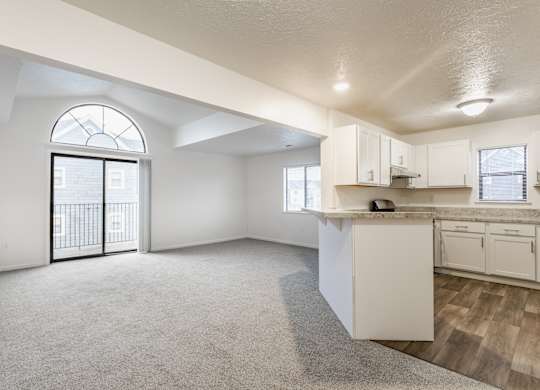 A spacious, empty room with a kitchenette and a large window with a view of a balcony at Huntington Cove Apartments, Merrillville, IN, 46410