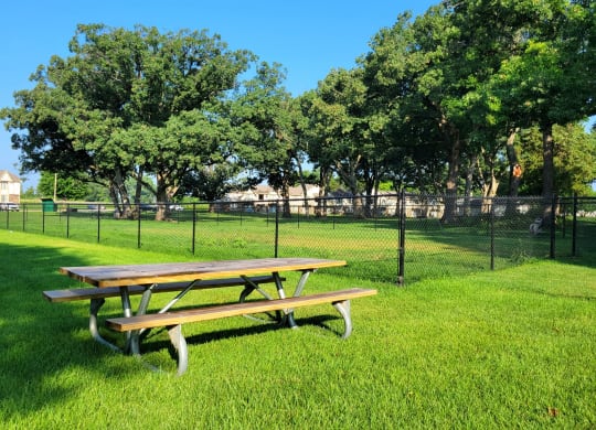 a picnic table in a grassy field with a chain link fence in the background at Beacon Hill and Great Oaks Apartments, Illinois
