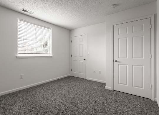 an empty living room with a white door and a window at Latitudes Apartments, Indianapolis, IN