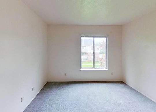 A bedroom with a window and carpeted floor at Briarwood Apartments in Benton Harbor, MI