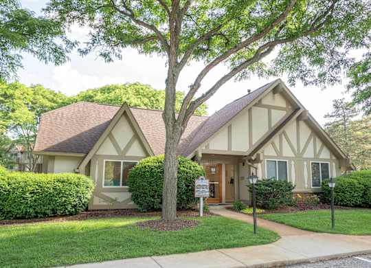 A house with a brown roof and white trim is surrounded by greenery.