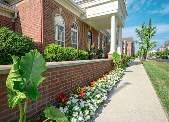 A brick building with a white porch and a flower bed in front at Alexandria of Carmel Apartments, Carmel, Indiana