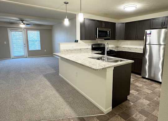 A kitchen with a breakfast bar and a living room at Andover Pointe Apartment Homes in LaVista, NE
