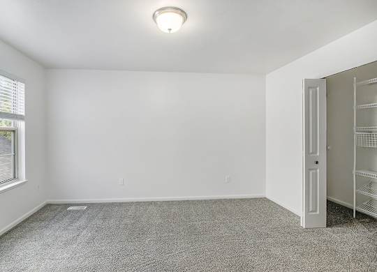 A room with a carpeted floor, a window with blinds, a door, and a ceiling light fixture at Autumn Lakes Apartments and Townhomes, Mishawaka, 46544