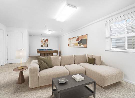 A basement recreation room with a beige couch, a coffee table, and a lamp at Autumn Lakes Apartments and Townhomes, Mishawaka, 46544
