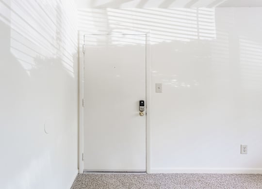 A white door with a black handle and lock in a white room