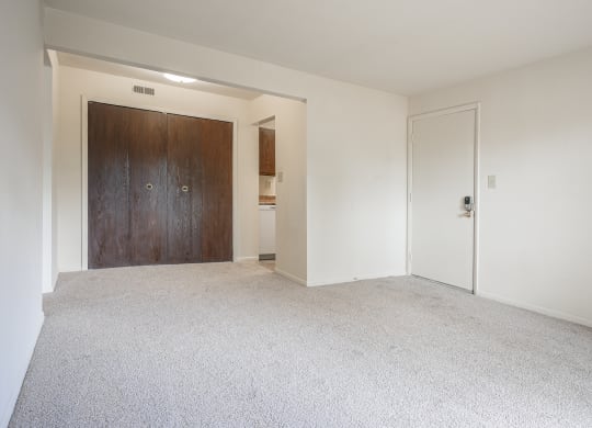 an empty living room with white carpet and a wooden door at Bavarian Village Apartments, Indianapolis, IN