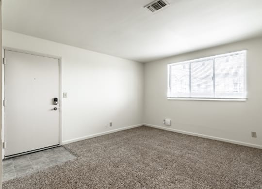 an empty room with carpet and a window and a door at Bay Pointe Apartments in Lafayette, IN