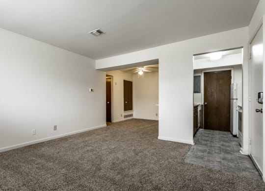an empty living room with white walls and carpeting and a door to a kitchen at Bay Pointe Apartments in Lafayette, 47909