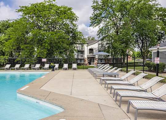 A pool surrounded by trees and lounge chairs.