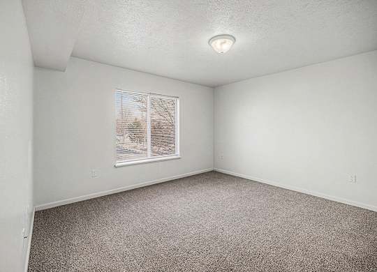 A bedroom with a large window and carpeted floor at Brentwood Park Apartments in LaVista, NE