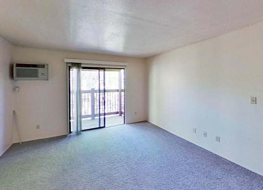 A living room with a carpeted floor and a sliding glass door leading to a balcony at Briarwood Apartments in Benton Harbor, MI
