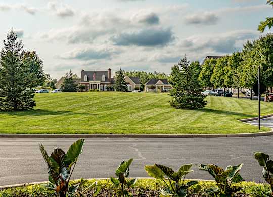 A large building is surrounded by a green lawn and trees