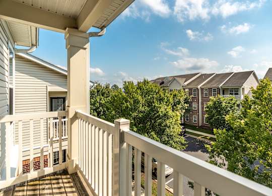 A balcony with a white railing overlooks a street with houses and trees
