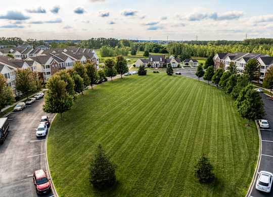 A large grassy area surrounded by apartment buildings and cars parked in a lot