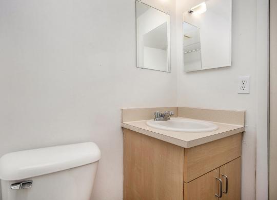A toilet sits next to a sink with a mirror above it in a bathroom at Brookside Apartments, Springfield