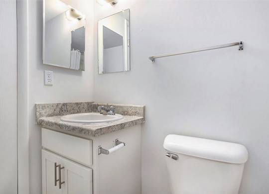 A bathroom with a white cabinet, sink, mirror, toilet and towel bar at Brookside Apartments, Springfield