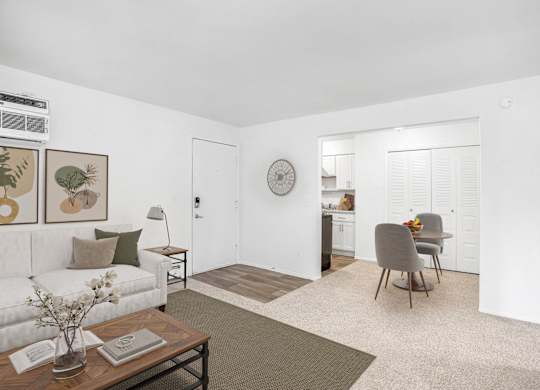 A living and dining room with a couch, a chair, a table, and a clock on the wall at Brookside Apartments, Springfield