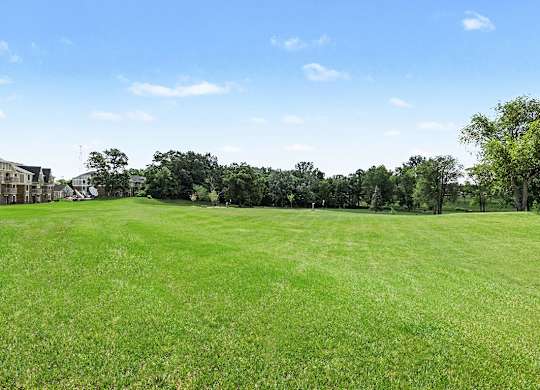 A large grassy field with trees and houses in the background.