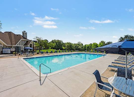 A large outdoor swimming pool surrounded by sun loungers and umbrellas.