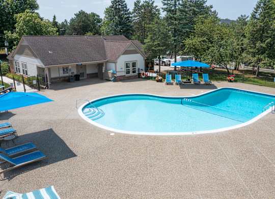 A large outdoor swimming pool surrounded by a shaded area and a building.