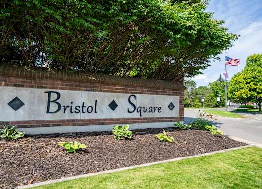 A sign that says Bristol Square is in front of a brick wall.