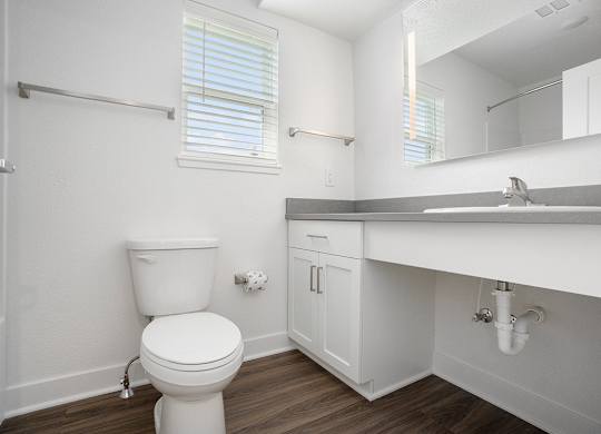 A bathroom with a window, toilet with a white cabinet and sink at Byron Lakes Apartments, Byron Center, Michigan