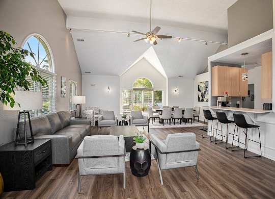 A community room with a grey sofa, armchairs and a kitchen with breakfast bar at Canal 2 Apartments in Lansing, MI