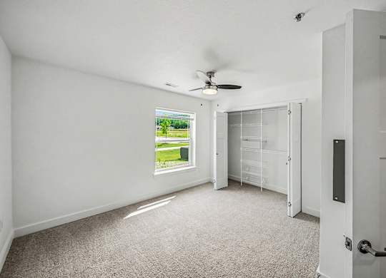 A room with a ceiling fan and a window showing a green lawn outside.