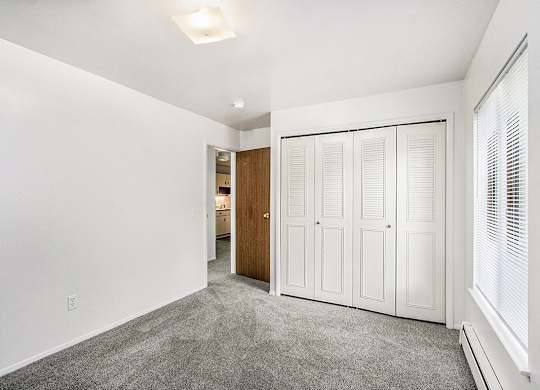 A bedroom with a large window and a grey carpet at Concord Place Apartments, Kalamazoo, MI